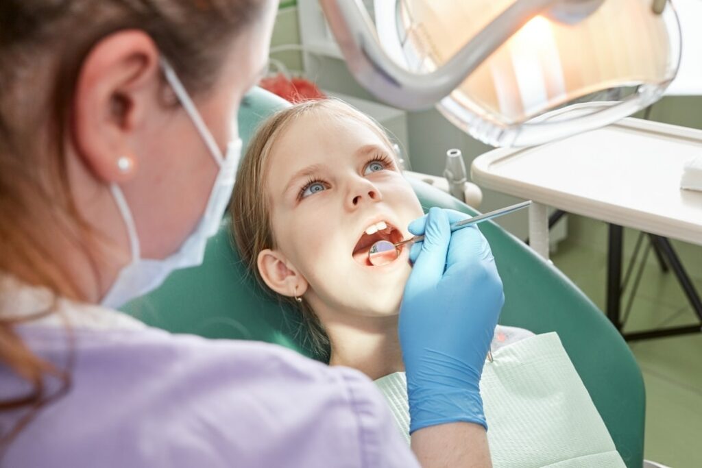 Child to the dentist. Child in the dental chair dental treatment during surgery. Small patient visiting specialist in dental clinic.