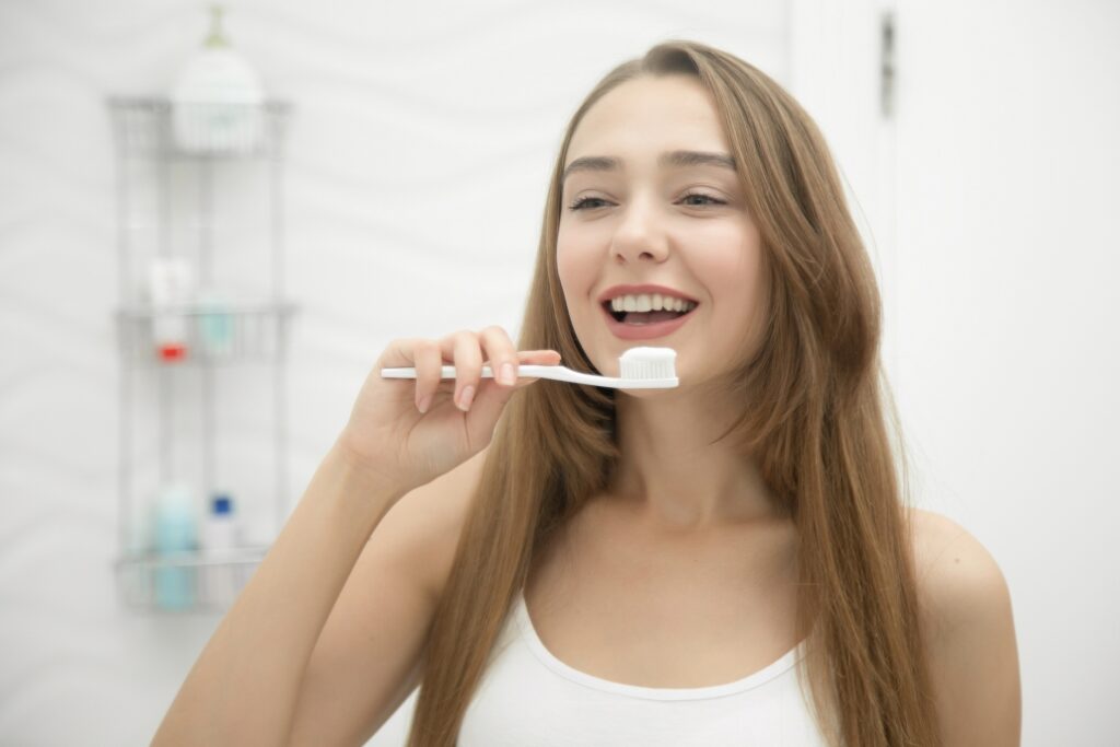 Portrait of a young smiling girl cleaning her teeth, looking at the bathroom mirror. Lifestyle, beauty concept photo